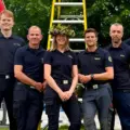 Fem personer står uppradade framför en midsommarstång